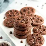 A stack of soft Vegan Double Chocolate Cookies with melty chocolate chips and crispy edges on a baking sheet
