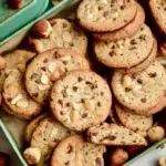 Freshly baked Vegan Hazelnut Cookies topped with chopped nuts and dark chocolate chips on a parchment-lined tray