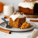 A slice of moist Vegan Pumpkin Cake on a white plate with autumn decorations in the background