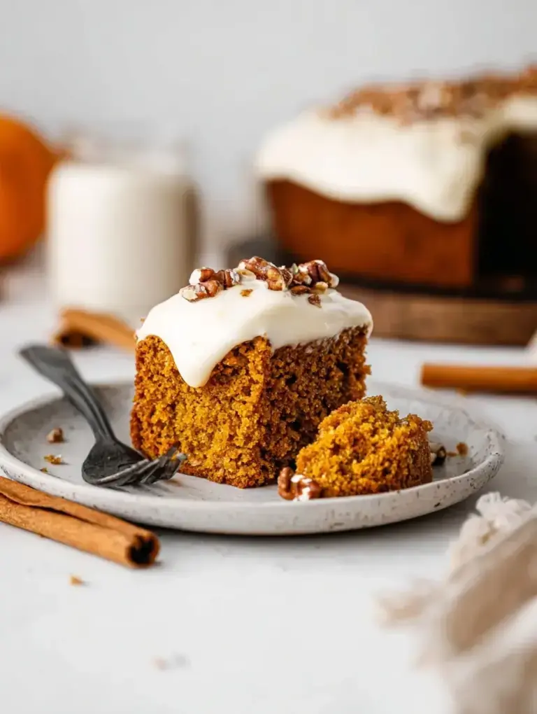 A slice of moist Vegan Pumpkin Cake on a white plate with autumn decorations in the background