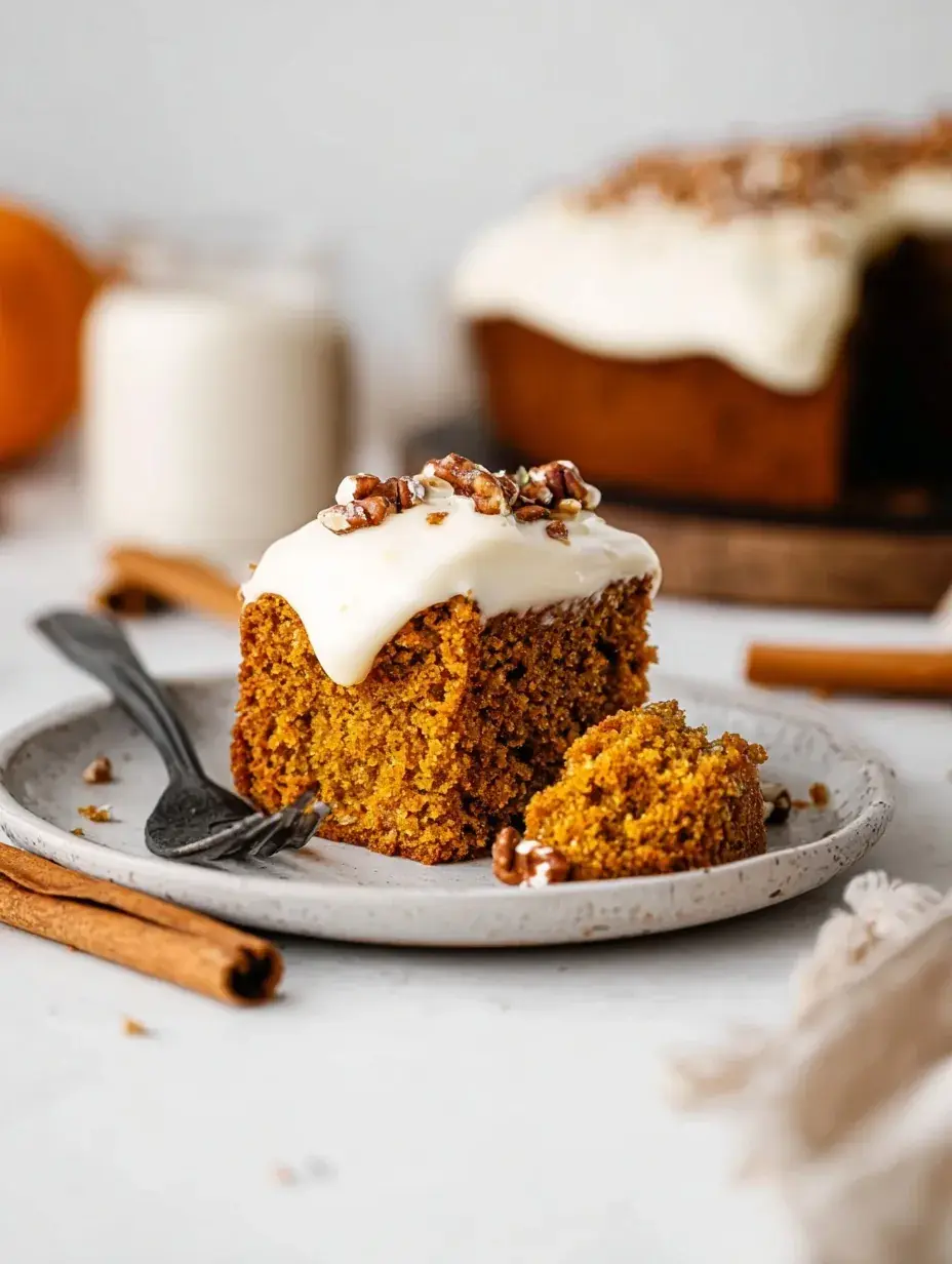 A slice of moist Vegan Pumpkin Cake on a white plate with autumn decorations in the background