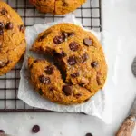 A pile of Vegan Pumpkin Chocolate Chip Cookies with melty chocolate chips on a wire rack.