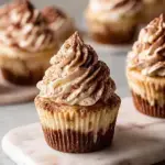 A tray of Vegan Tiramisu Cupcakes with white frosting and a dusting of cocoa powder on a wooden table.
