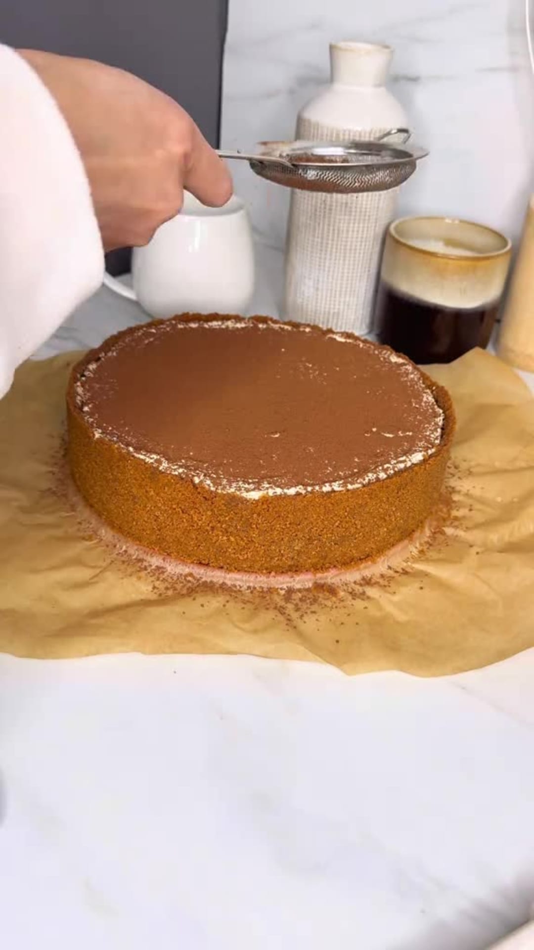 No-Bake Speculoos Tiramisu Cheesecake - Dusting cocoa powder over cake